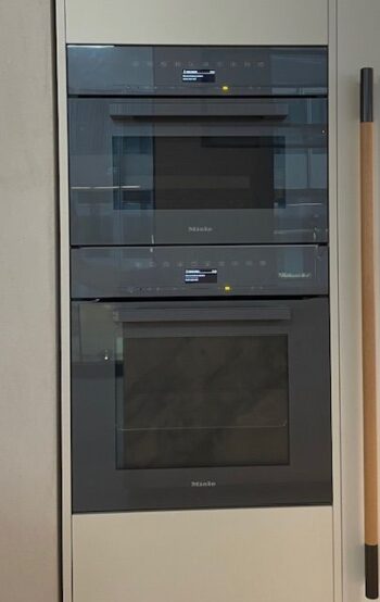 Molteni Abverkauf, Outlet, Angebot: Kücheneinbaugeräte, darunter zwei Backöfen und eine Mikrowelle, sind in einem modernen Molteni&C-Küchenschrank vertikal neben einem Besen gestapelt.