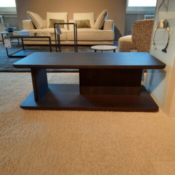 Ein rechteckiger Couchtisch „Hugo Beistelltisch“ aus dunklem Holz mit offenem Regal steht auf einem hellen Teppich, eingerahmt von einem beigen Sofa und anderen Möbeln von Molteni&C im Hintergrund.