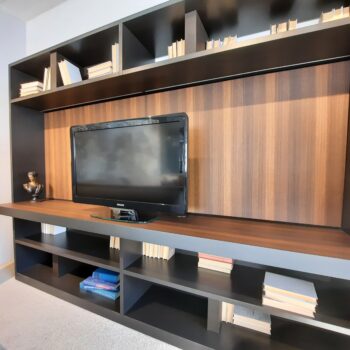 Ein Flachbildfernseher steht auf einer Molteni&C 505 Wohnwand-Unterhaltungseinheit mit Regalen, in denen Bücher und eine kleine Büste hängen. Der Hintergrund ist mit einer eleganten Holzvertäfelung versehen.