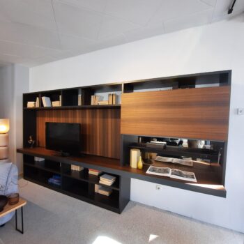 Eine moderne 505 Wohnwand von Molteni&C, an der Wand montiert und mit einem Fernseher, Büchern, Dekorationsartikeln und einem offenen Buch, elegant präsentiert auf einer dunklen Holzoberfläche.