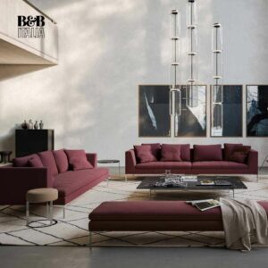 Modernes Wohnzimmer von Braum Interior Design mit kastanienbraunen Sofas, einer Bank, einem Couchtisch aus Glas, abstrakter Wandkunst, großen Pendelleuchten und einem hellen geometrischen Teppich. B&B Italia Logo in der oberen linken Ecke. Räume die wirken - Interior Design 2026 Inspiration.
