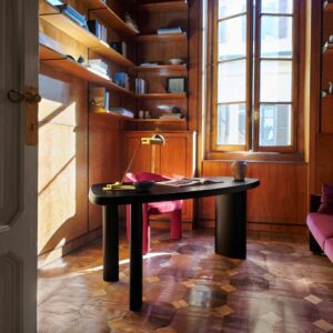Ein Homeoffice zum schön wohnen: Holzwände und Regale, großes Fenster, schwarzer Schreibtisch mit Lampe, Büchern und Vase sowie ein roter Stuhl auf gemustertem Parkett - perfekt, um besser arbeiten zu können.