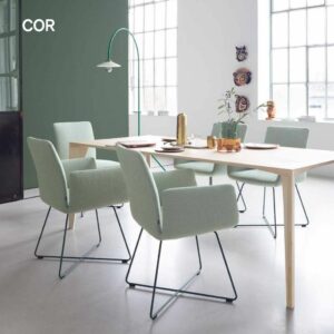 Ein moderner Essbereich von Braum Interior Design mit einem hellen Holztisch, vier hellgrünen Stühlen, stilvollem Geschirr, einer Pflanze, Wandkunst und großen Fenstern, die natürliches Licht hereinlassen - perfekt für helle Räume in Interior Design 2026.