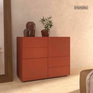 Ein moderner roter Schrank mit klaren Linien, dekoriert mit zwei Glasvasen und einer Pflanze, steht vor einer beigen Wand in der Nähe eines großen Spiegels - ein Beispiel für raffiniertes Interior Design in stilvollen Räumen.