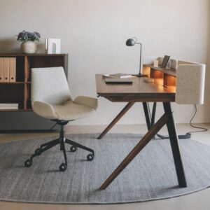 Ein modernes Homeoffice mit Holzschreibtisch, ergonomischem Stuhl, Lampe, Regalen, Büchern und einer Blumenvase auf rundem grauen Teppich - perfekt zum besser arbeiten und schön wohnen.