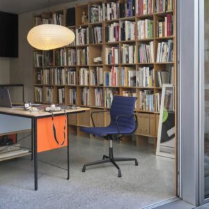 Ein modernes Homeoffice mit Schreibtisch, Drehstuhl, mit Büchern gefüllten Regalen, Laptop, Kaffeetasse und einer runden Hängelampe - ideal für schön wohnen und besser arbeiten.