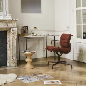 Ein modernes Home Office mit rotem Drehstuhl, hölzernem Beistelltisch und Marmorkamin strahlt Harmonie zu Hause aus. Aufgeschlagene Bücher und Zeitschriften, die auf dem Holzboden verstreut liegen, laden in dieser hellen Vitra Homestories Umgebung zur gemütlichen Winterinspiration ein.