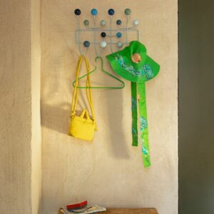 Eine Wandgarderobe von Vitra, ein echter Designklassiker, hält einen grünen Sonnenhut, eine gelbe Tasche und einen grünen Kleiderbügel; Zeitschriften und Sonnenbrillen liegen auf einer Holzbank darunter.