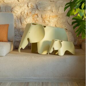 Zwei minimalistische gelbe Elefanten-Skulpturen von Vitra, eine große und eine kleine, stehen auf einer Steinstufe neben einem Sofa und einer Grünpflanze, die die strukturierte Steinwand akzentuieren - perfekte Akzente von Möbel Braum für jeden Designklassiker-Liebhaber.