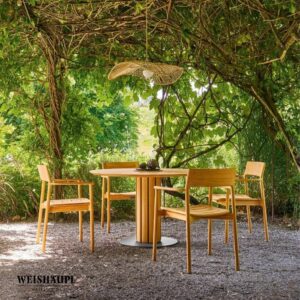 Vier Holzstühle und ein runder Tisch stehen unter einer mit Weinreben bewachsenen Pergola mit einer geflochtenen Leuchte. So entsteht ein einladender Sitzbereich im Freien, der den zeitlosen Touch von Braum Interior Design-Räume die wirken widerspiegelt.