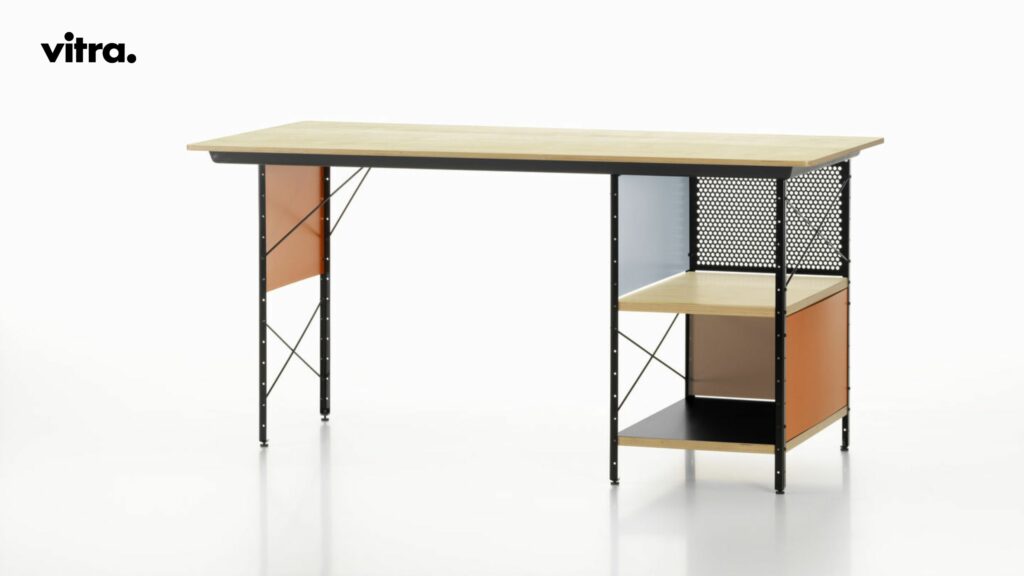 Ein minimalistischer Schreibtisch mit einer Tischplatte aus hellem Holz, schwarzen Metallbeinen, farbigen Paneelen und offenen Regalen vor weißem Hintergrund. In der oberen linken Ecke ist das Vitra-Logo zu sehen. Dieser Eames-Schreibtisch eignet sich perfekt für Ihre „Vitra Back to School“-Einrichtung und lässt sich nahtlos mit dem ikonischen Eames Fiberglass Chair kombinieren, um einen stilvollen und funktionalen Arbeitsplatz zu schaffen.
