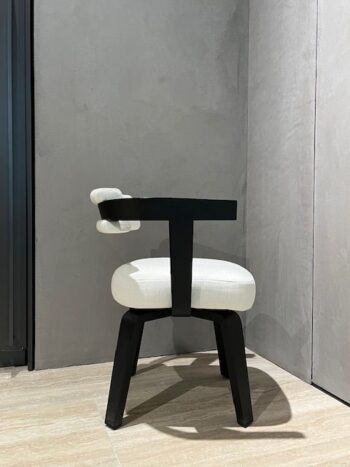 Ein moderner Porta Volta Stühle von Molteni&C mit weiß gepolstertem Sitz und Rückenlehne, schwarzem Gestell und abgewinkelten Beinen steht vor einer grauen Wand auf einem hellen Holzboden. Auch als 4er Set erhältlich.