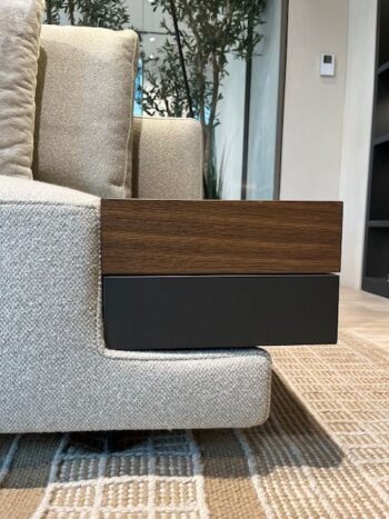 Eine Nahaufnahme des Marteen Sofas, ein Designersofa von Molteni&C, mit beigem Bezug und einem eingebauten Beistelltisch aus Holz und schwarzem Metall, der an der Armlehne befestigt ist und auf einem gemusterten Teppich steht.