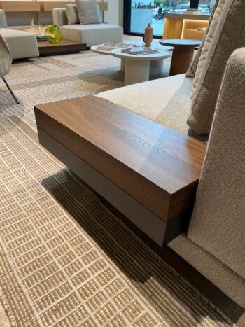 Ein modernes Wohnzimmer mit einem beigen Marteen-Sofa von Molteni&C, einer eingebauten Armlehne aus Holz, strukturiertem Teppichboden und einem runden weißen Couchtisch mit Zeitschriften.
