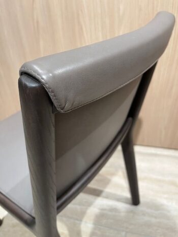 Nahaufnahme eines modernen Janet Stuhls mit gepolsterter, grauer Lederrückenlehne und Sitzfläche, dunklem Holzrahmen und hellem Holzhintergrund - Teil eines eleganten 4er-Sets von Molteni&C.