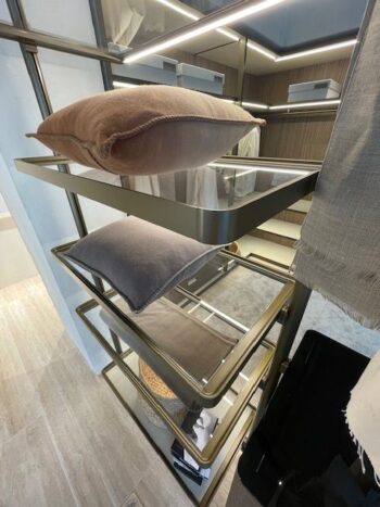 Ein modernes Ankleidezimmer mit Glasregalen von Molteni&C zeigt zwei Kissen, während auf den unteren Regalen Kleidung und geflochtene Körbe fein säuberlich angeordnet sind.