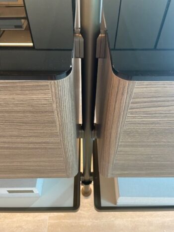 Nahaufnahme von zwei Molteni&C Hector Night Holzschränken mit schwarzen Glasplatten, die nebeneinander stehen und durch einen vertikalen Metallträger getrennt sind - eine elegante Ergänzung für jedes Ankleidezimmer.