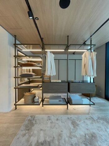 Moderner begehbarer Kleiderschrank mit offenen Regalen, hängenden Kleidungsstücken, Aufbewahrungsboxen, gefalteten Handtüchern, einem Korb und einem Design aus hellem Holz und Metall von Molteni&C Ankleide. Im Vordergrund ist der Teppichboden zu sehen.