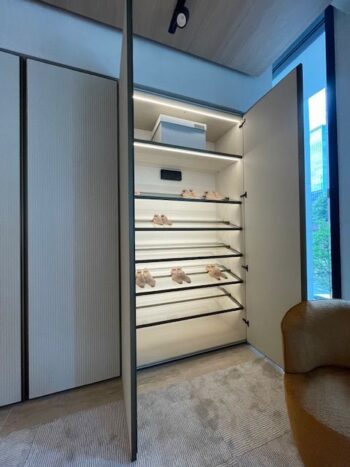 Ein großer offener Gliss-Master-Schrank von Molteni&C mit beleuchteten Einlegeböden zeigt mehrere Paar beigefarbene Schuhe, eine weiße Schachtel auf dem obersten Regal und einen modernen Stuhl im Vordergrund - perfekt für jedes moderne Ankleidezimmer.