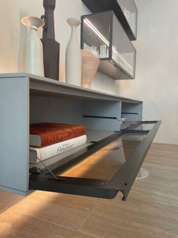 Ein moderner grauer Schrank von Wandmodul aus der Kollektion Pass-Word Evolution von Molteni&C verfügt über eine Glastür, die sich öffnen lässt, um zwei Bücher zu enthüllen, während dekorative Vasen und Töpferwaren die Oberseite zieren.