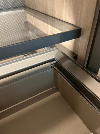Nahaufnahme einer Schublade von Molteni&C Gliss Master mit Details aus Metall und beigem Leder, teilweise geöffnet unter einer Glasablage mit Holzpaneel im Hintergrund.