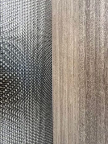 Eine Nahaufnahme zweier nebeneinander liegender Oberflächen: Eine Seite weist ein strukturiertes, schwarzes Webmuster auf, während die andere eine glatte, hellbraune Holzmaserung zeigt - beides Elemente, die das raffinierte Design des Gliss Master Kleiderschranks von Molteni&C widerspiegeln.