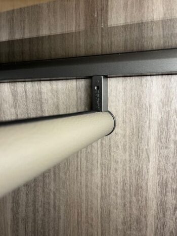 Eine Metallstange wird mit einer schwarzen Halterung horizontal an der Wand befestigt und steht vor einer holzgemusterten Oberfläche, die an das elegante Design des Gliss Master Kleiderschranks von Molteni&C erinnert.