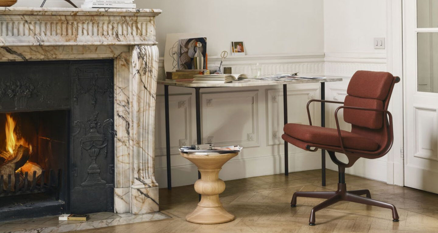 Ein modernes Heimbüro mit einem braunen Drehstuhl, einem hölzernen Beistelltisch, einem Marmorkamin und einem Schreibtisch mit Büchern und Dekorationsgegenständen.
