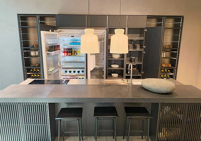 Moderne Molteni&C-Küche mit einer Insel, drei Hockern, einem Mittelstück aus Stein, einem offenen Kühlschrank mit Getränken und offenen Schränken mit Geschirr und Weinflaschen. Die Ratio Essenza Küche ist elegant mit hochwertigen Küchengeräten ausgestattet.