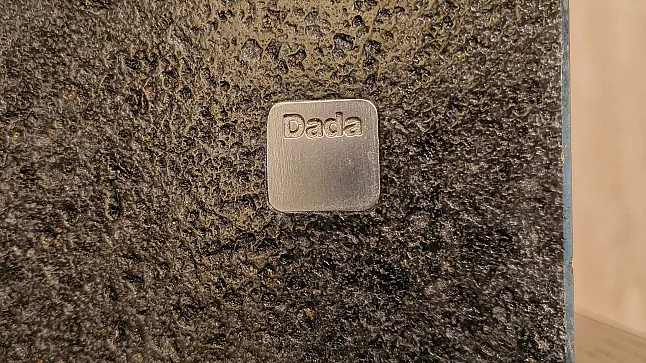 Quadratische Metallplatte mit dem Wort Dada auf einer strukturierten schwarzen Oberfläche, ein raffiniertes Detail, das häufig bei Molteni&C-Designs und Premium Ratio Essenza Küchengeräten zu finden ist.