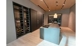 Molteni Abverkauf, Outlet, Angebot: Moderne Küche mit Ratio Essenza Küche von Molteni&C, mit minimalistischen dunklen Schränken, eingebautem Weinregal, zentraler Insel mit Spüle, hochwertigen Küchengeräten und stilvoller Hängebeleuchtung auf einem hellen Holzboden.