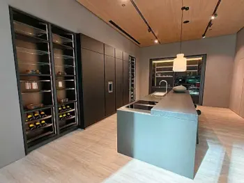 Molteni Abverkauf, Outlet, Angebot: Moderne Küche mit Ratio Essenza Küche von Molteni&C, mit minimalistischen dunklen Schränken, eingebautem Weinregal, zentraler Insel mit Spüle, hochwertigen Küchengeräten und stilvoller Hängebeleuchtung auf einem hellen Holzboden.