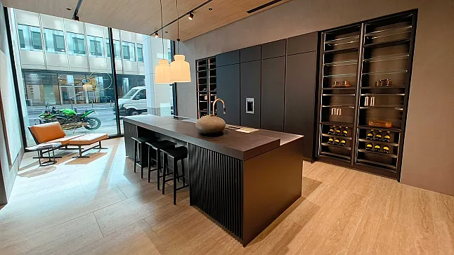 Moderne Küche mit einer Molteni&C Ratio Essenza Küche, großer schwarzer Insel, eleganten Küchengeräten, Barhockern, eingebauten Regalen mit Weinflaschen, Sessel am Fenster und Blick auf die Straße.