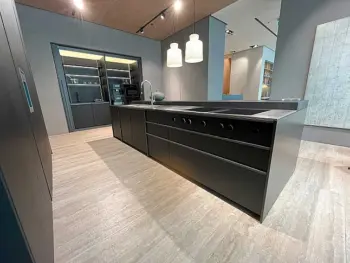Molteni Abverkauf, Outlet, Angebot: Moderne Küche mit mattschwarzer Insel, eingebautem Kochfeld und hochwertigen Küchengeräten, minimalistischen Schränken, Hängeleuchten und offenen Regalen. Helle Holzböden und neutrale Wände schaffen die perfekte Ratio Essenza Küche von Molteni&C.