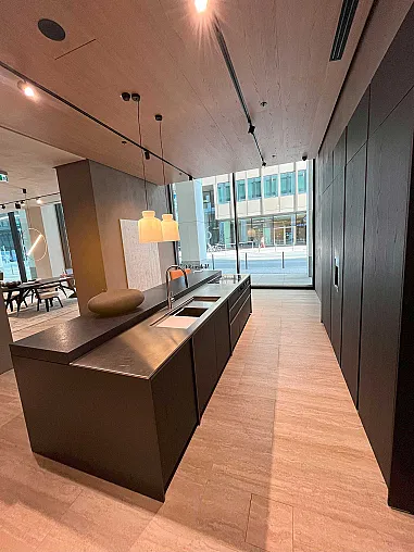 Moderne Küche mit dunklen Schränken, Molteni&C-Insel mit eingebauter Spüle, Pendelleuchten und großen, raumhohen Fenstern mit Blick auf eine Stadtstraße. Das Design von Ratio Essenza Küche hebt hochwertige Küchengeräte hervor.