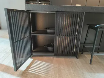Molteni Abverkauf, Outlet, Angebot: Ein moderner schwarzer Molteni&C-Küchenschrank mit Lamellentüren ist geöffnet und gibt den Blick frei auf zwei elegante Küchengeräte in den Regalen. Das Sonnenlicht wirft elegante Schatten auf den Boden.