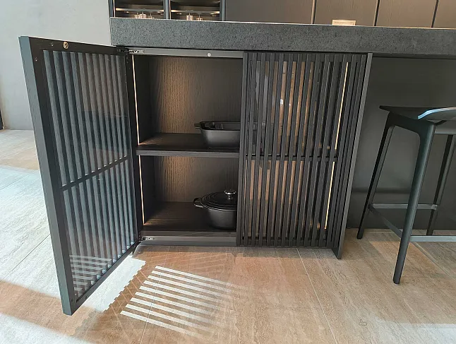 Ein moderner schwarzer Molteni&C-Küchenschrank mit Lamellentüren ist geöffnet und gibt den Blick frei auf zwei elegante Küchengeräte in den Regalen. Das Sonnenlicht wirft elegante Schatten auf den Boden.