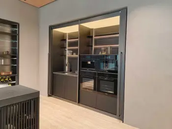 Molteni Abverkauf, Outlet, Angebot: Moderne Küche mit schwarzen Molteni&C-Einbauschränken, einer Spüle, offenen Regalen mit Geschirr und integrierten Küchengeräten wie Backofen und Mikrowelle - alles vor einer hellen Wand und einem hellen Boden.
