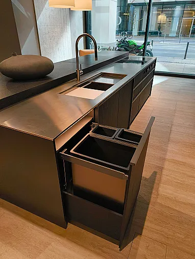 Moderne Molteni&C Ratio Essenza Küche mit einer Arbeitsplatte aus Edelstahl, einem Waschbecken, einem Wasserhahn und einer offenen Schublade mit eingebauten Abfall- und Recyclingbehältern. Ein großes Fenster mit Blick auf die Straße vervollständigt den eleganten Look, perfekt für die Präsentation von Küchengeräten.