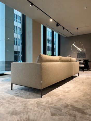 Der moderne Loungebereich ist mit einem beigen Molteni&C Paul Sofakombi auf einem hellen Teppich ausgestattet, mit großen, raumhohen Fenstern, einer runden Leuchte und einem minimalistischen Esstisch im Hintergrund.