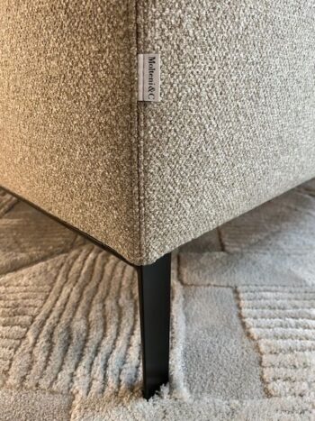 Nahaufnahme einer strukturierten beigen Paul Sofa-Ecke von Molteni&C mit einem Stoffanhänger von Monet & Co., schwarzen Metallbeinen und einem gemusterten hellen Teppich darunter.