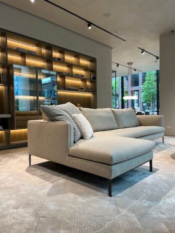 Ein modernes Molteni&C Paul Sofakombi-Sofa mit Kissen liegt auf einem strukturierten Teppich in einem modernen Wohnzimmer mit eingebauten Regalen und großen Fenstern.