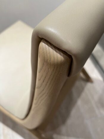 Nahaufnahme eines beigefarbenen, gepolsterten Yoell Stuhls mit Holzgestell, wobei die geschwungene Rückenlehne und die glatte Polsterung im Mittelpunkt stehen - ein raffiniertes Design von Molteni&C.