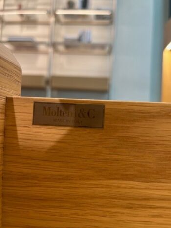 Nahaufnahme eines Molteni&C-Etiketts aus Metall auf einem hölzernen Sideboard mit der Aufschrift 