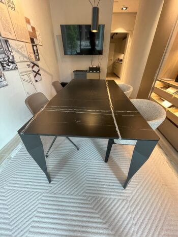 Ein moderner Diamond Designtisch mit einer schwarzen Marmorplatte mit weißer Maserung, umgeben von vier Molteni&C Stühlen in einem modernen Raum mit Wanddisplays und einem Fernseher.