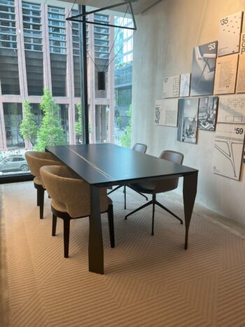 Ein moderner Diamond Designtisch mit vier Stühlen steht auf einem hellen Teppich in der Nähe der bodentiefen Fenster. An der Wand daneben hängen die Designposter von Molteni&C.