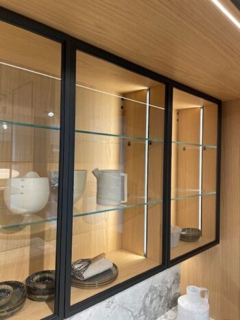 Molteni Abverkauf, Outlet, Angebot: In den gläsernen Küchenschränken aus Molteni&C-Holz mit schwarzem Rahmen werden weiße Keramikkrüge, Schalen und schwarzes Geschirr auf Glasböden präsentiert. Unten ist die elegante Arbeitsplatte aus Intersection-Marmor zu sehen.