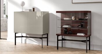 Zwei moderne Schränke auf schwarzen Metallbeinen stehen nebeneinander; der eine ist geschlossen und in glänzendem Beige gehalten, der andere offen mit Glastüren, die dekorative Gegenstände zeigen.