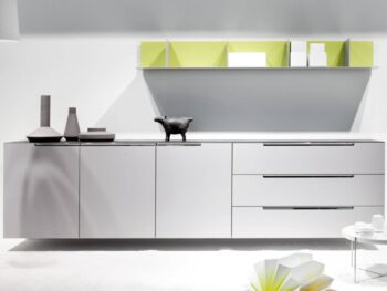 Minimalistisches Sideboard Mell von Interlübke mit drei Schubladen, zwei Schränken, dekorativen Vasen, einer schwarzen Tierfigur, einem schwebenden Regal mit grünen Trennwänden und einem niedrigen Tisch mit offenen Büchern.