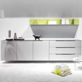 Minimalistisches Sideboard Mell von Interlübke mit drei Schubladen, zwei Schränken, dekorativen Vasen, einer schwarzen Tierfigur, einem schwebenden Regal mit grünen Trennwänden und einem niedrigen Tisch mit offenen Büchern.
